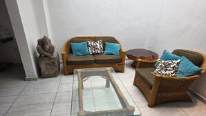 Un salon aménagé avec une table basse en verre, des canapés en osier dotés de coussins bleus et une sculpture en pierre.