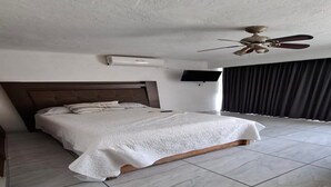 Une chambre d’hôtel avec un grand lit, un ventilateur de plafond, un téléviseur à écran plat et une vue sur l’extérieur.