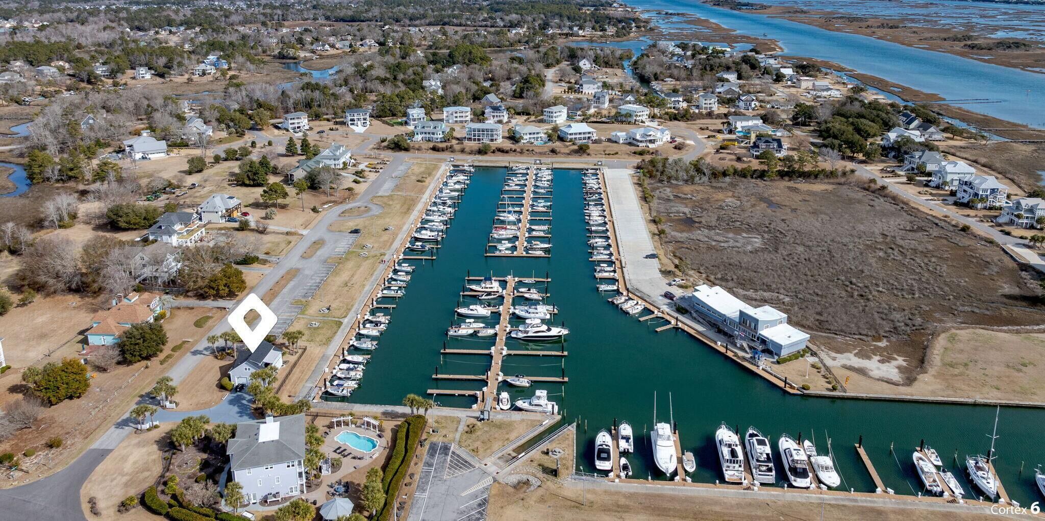 An aerial view of a marina with numerous docks and boats, surrounded by residential houses and a small building.