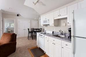 Cocina moderna con armarios blancos, estufa, microondas y refrigerador. Cuenta con un comedor con mesa y sillas.
