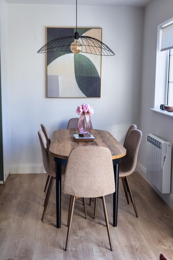 A dining area with a wooden table, six chairs, a vase with flowers, a hanging light fixture, and a radiator. - Cosy 3-Bedroom Home in Beautiful Killarney (Killarney)