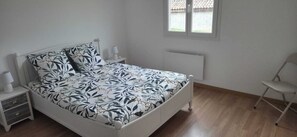 Ein Schlafzimmer mit Bett, Nachttischen, einem Sessel und einem Fenster mit Blick auf ein Gebäude.