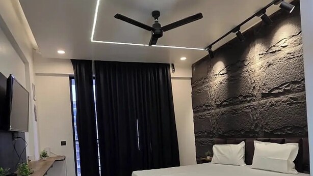 A modern bedroom with a bed, ceiling fan, and a stone wall. - Omex Hazratganj (Lucknow)