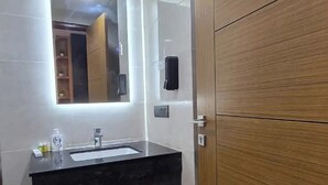 A bathroom with a dark marble sink, a mirror above it, and a wooden door. - Omex Hazratganj (Lucknow)
