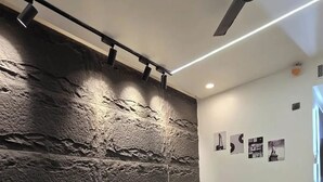 A modern bedroom with a large bed, a ceiling fan, and a textured wall. - Omex Hazratganj (Lucknow)