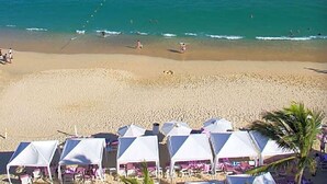 Una playa con tiendas de campaña blancas y sillas reclinables, una orilla arenosa y el océano.