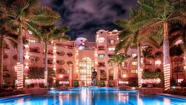 Un hotel con una piscina grande, palmeras y cielo nocturno.