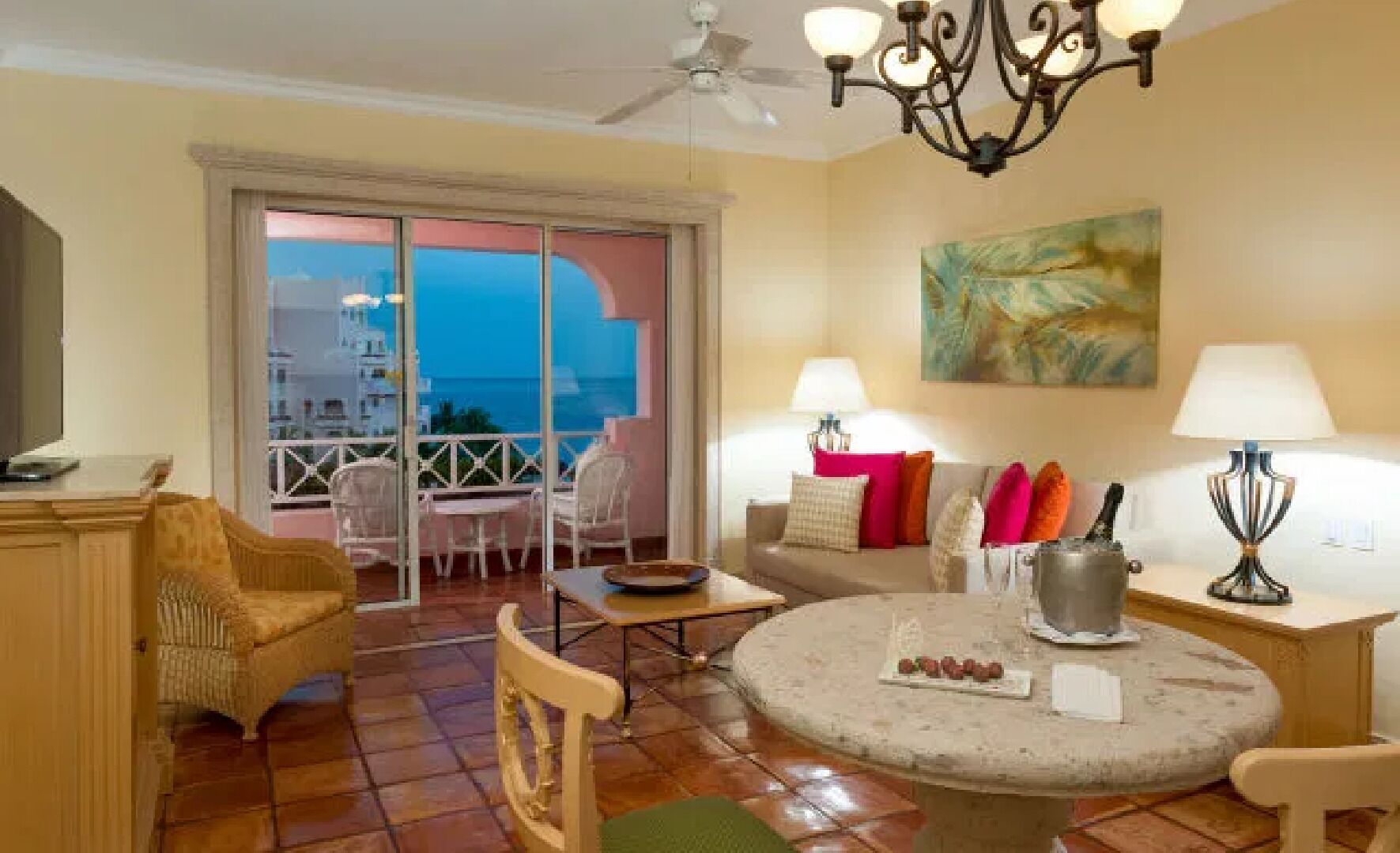 Ein Wohnzimmer mit Balkon, einem runden Tisch mit Snacks, einer Couch mit Kissen und einem Gemälde an der Wand.