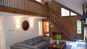 A spacious living area with a large gray sectional sofa, a wooden staircase, and a view of the outdoors. - Poconos-Four Season Amenities-Game Room-Fire Pit-Hot Tub-Ski  (Bushkill)
