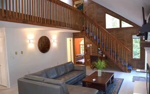 A spacious living area with a large gray sectional sofa, a wooden staircase, and a view of the outdoors. - Cozy Mountain Escape-Poconos-Four Season Amenities-Game Room-Fire Pit-Hot Tub (Bushkill)