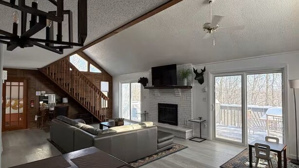 A spacious living room with a fireplace, a staircase, and a large window. - Poconos-Four Season Amenities-Game Room-Fire Pit-Hot Tub-Ski  (Bushkill)
