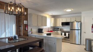 A modern kitchen with white cabinets, stainless steel appliances, and a wooden dining area with a bench. - Poconos-Four Season Amenities-Game Room-Fire Pit-Hot Tub-Ski  (Bushkill)