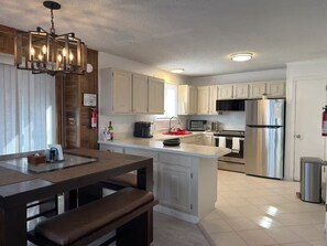 A modern kitchen with white cabinets, stainless steel appliances, and a wooden dining area with a bench. - Cozy Mountain Escape-Poconos-Four Season Amenities-Game Room-Fire Pit-Hot Tub (Bushkill)