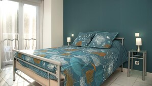 A bedroom with a bed, two bedside lamps, a window with curtains, and a view of the city. - Les Hirondelles - NEBOUZAT (NEBOUZAT)