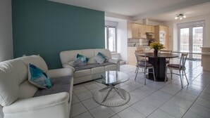 A modern living room with a sofa, a glass coffee table, and a dining area with a round table and chairs. - Les Hirondelles - NEBOUZAT (NEBOUZAT)