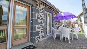 A stone building with a door and windows, a patio with a table and chairs, and a purple umbrella. - Les Hirondelles - NEBOUZAT (NEBOUZAT)