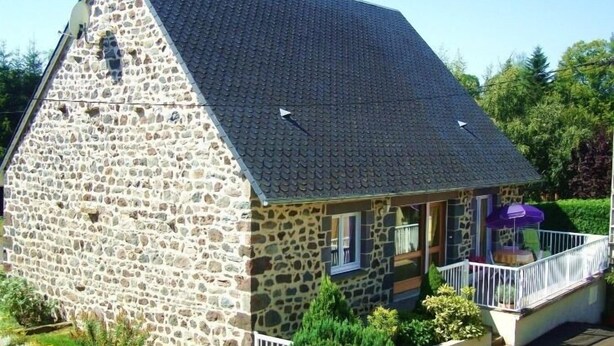A stone building with a steeply pitched roof, a porch with a railing, and a small garden area with shrubs and a pathway. - Les Hirondelles - NEBOUZAT (NEBOUZAT)