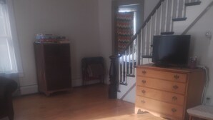 Una sala de estar con sofá, suelo de madera, escalera y televisor sobre un aparador.