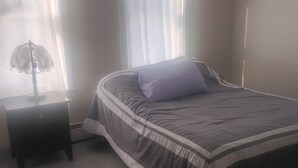 Un dormitorio con una cama, una mesita de noche y una ventana con cortinas.