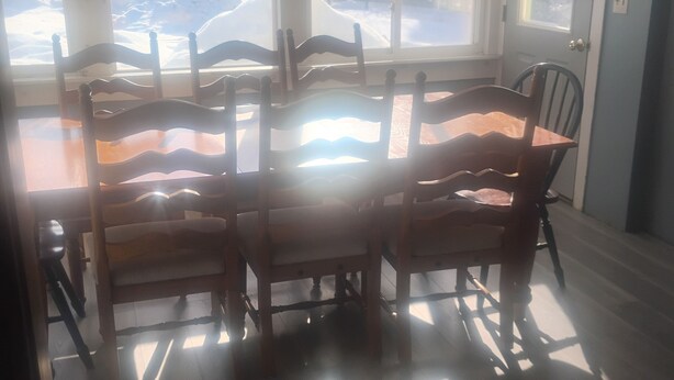 Un comedor con mesa y sillas de madera, ventanas amplias con vistas a un paisaje nevado, y una puerta a la derecha.