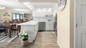 Une cuisine moderne avec des meubles blancs, un grand îlot central et un coin repas doté de tables et de chaises en bois.