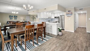 Une cuisine moderne avec des meubles blancs, un réfrigérateur en acier inoxydable et un coin repas comprenant des chaises en bois et un tapis à rayures.