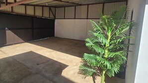 A spacious indoor area with a concrete floor, a metal roof, and a large potted plant. - Quesada House (Tamarindo)