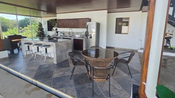 A modern kitchen with a large island, dark wooden cabinets, and a glass dining area. - Quesada House (Tamarindo)