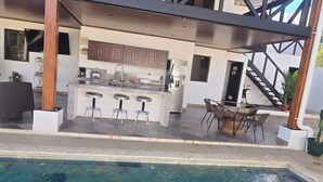 A modern kitchen with a central island, bar stools, and a dining area with chairs. - Quesada House (Tamarindo)