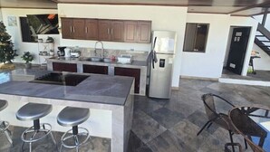 A modern kitchen with a central island, bar stools, a refrigerator, and wooden cabinets. - Quesada House (Tamarindo)