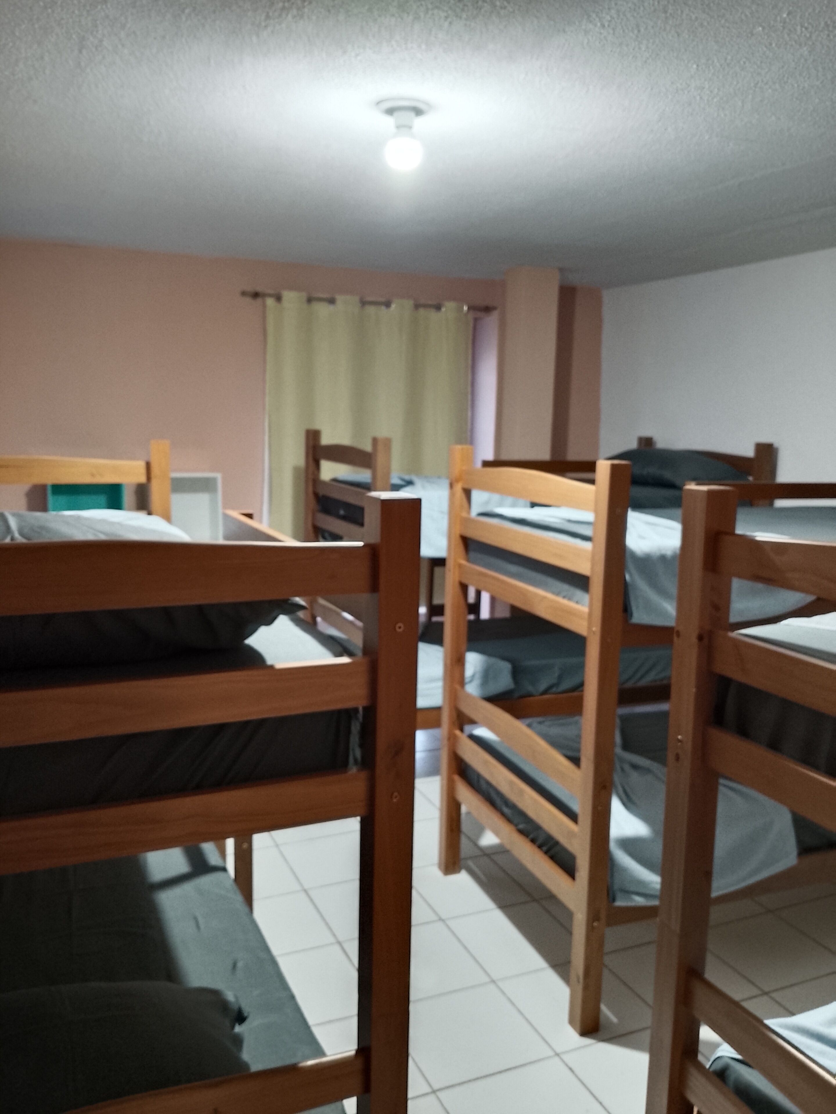 Ein Schlafsaalzimmer mit Etagenbetten, einer Deckenleuchte und einem Fenster mit Vorhängen.