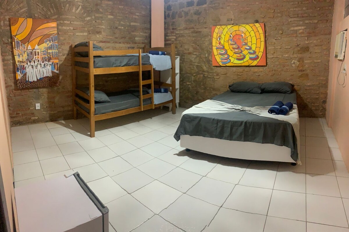 A room with a bunk bed, a single bed, tiled flooring, and two paintings on the walls.