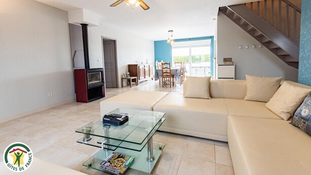 Een moderne woonkamer met een glazen salontafel, een beige bank en een trap.