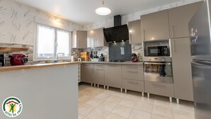 Een moderne keuken met een centraal eiland, roestvrijstalen apparatuur en een raam met zonwering.
