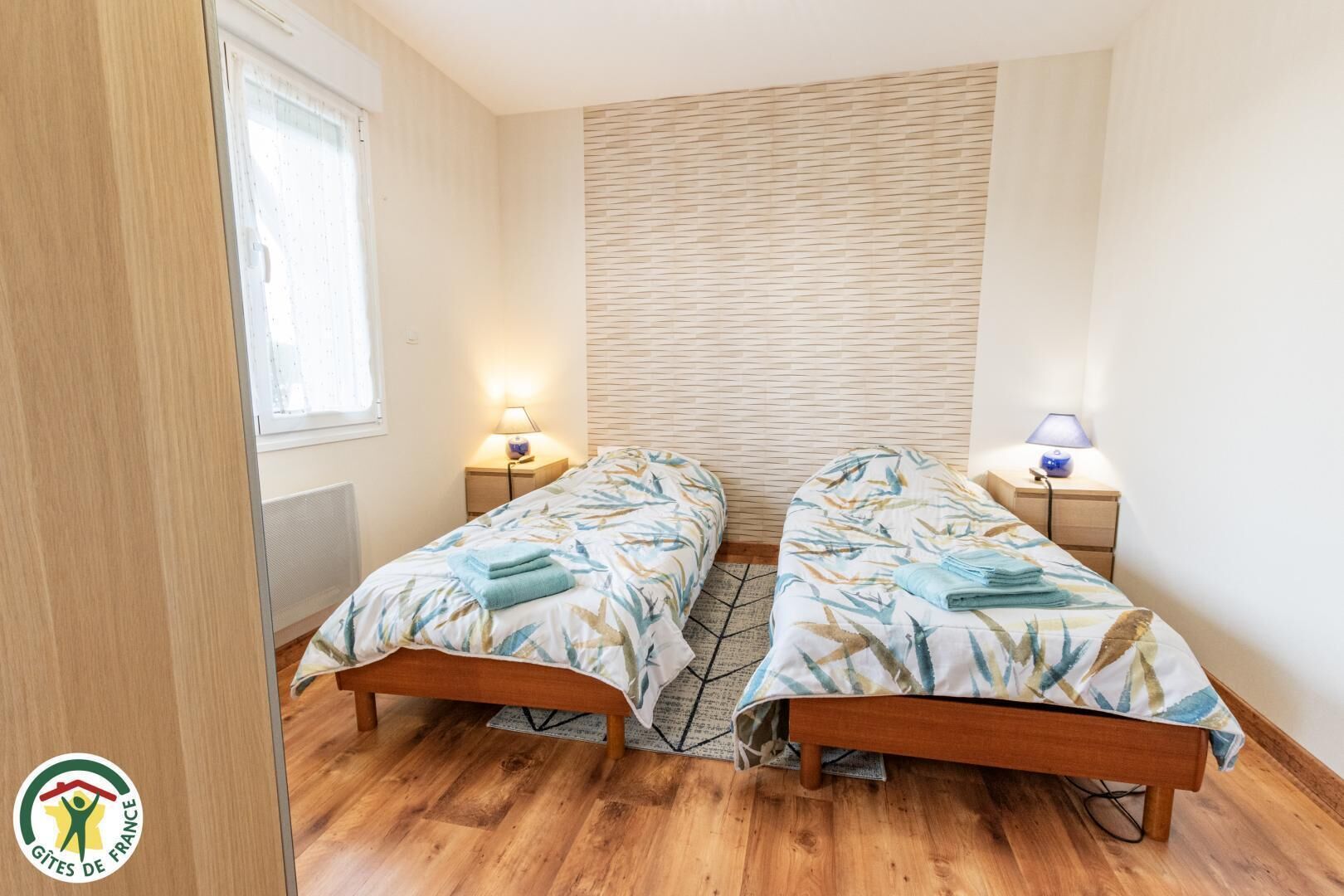 A bedroom with two single beds, wooden flooring, a brick-patterned wall, and bedside lamps.
