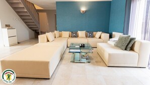 Een moderne woonkamer met een modulaire bank, een glazen salontafel en een trap naar een verdieping erboven.