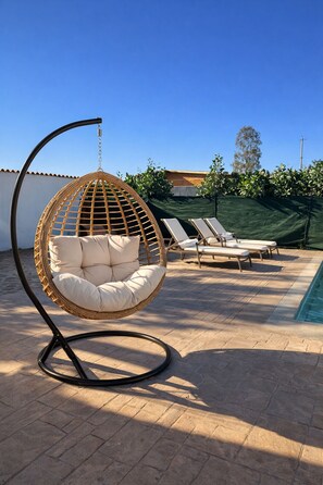 Silla colgante, sillones y un entorno junto a la piscina.
