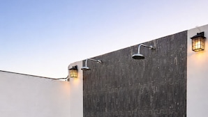 A modern outdoor shower area with a dark tiled wall, a tiled floor, and two wall-mounted lights. - HOTEL LARIMAR - Valle de Guadalupe (Valle de Guadalupe)