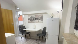 Een kleine keuken met een eettafel, twee stoelen, een koelkast en een kleine zwarte prullenbak.