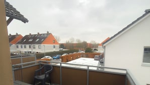 Een terras op het dak met een houten dek, een metalen hekwerk en een uitzicht op woongebouwen in de verte.