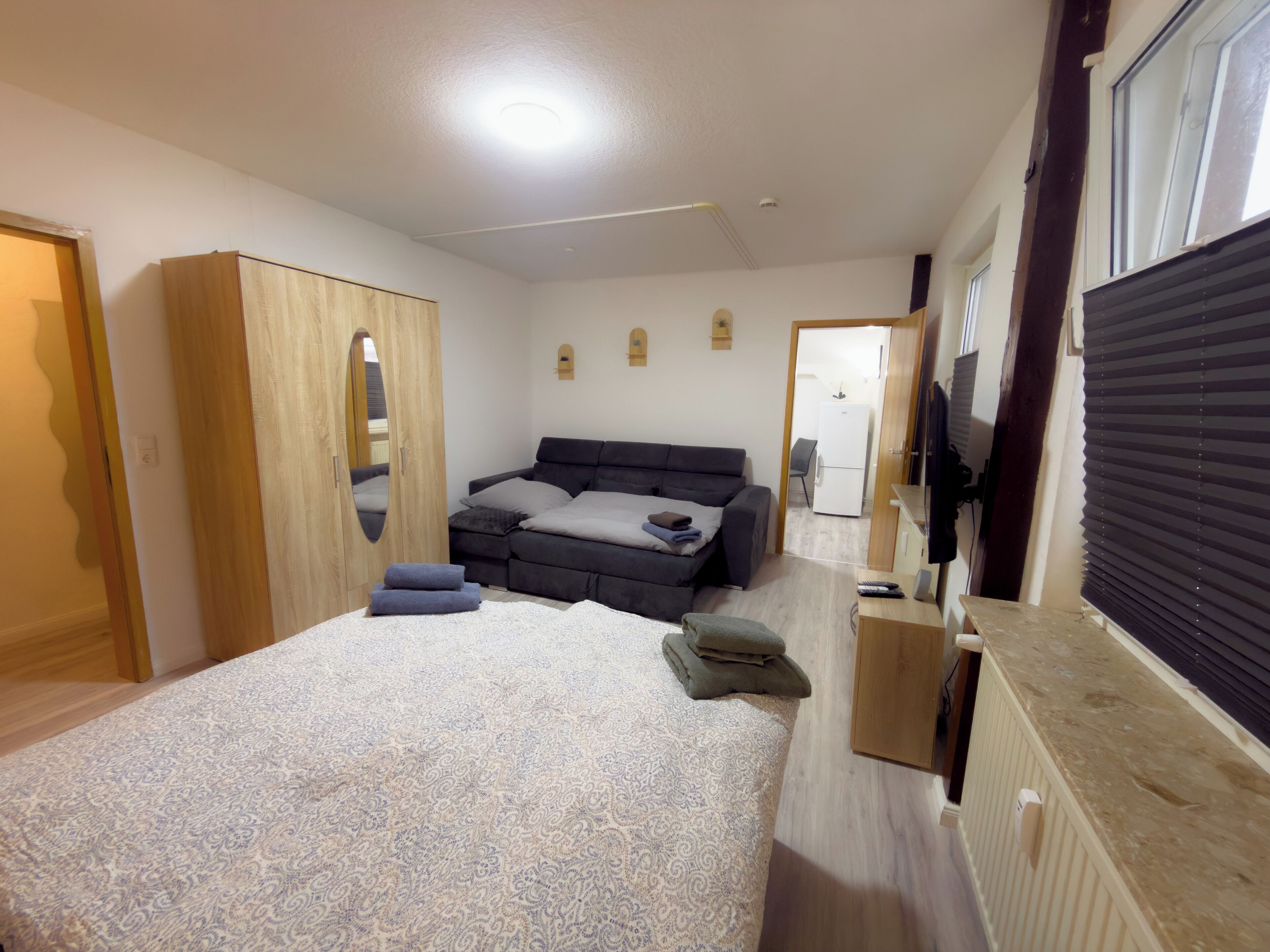 A bedroom with a bed, a wardrobe, a desk, and a television.