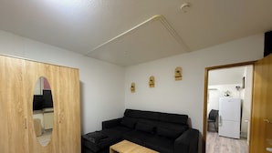 Een knus woongedeelte met een zwarte bank, een houten kast en een klein houten tafeltje.