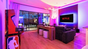 A modern living room with a large flat-screen TV displaying "NETFLIX," a wooden coffee table, a dark-colored sofa, and a glass door leading outside. - Oak Lawn Escape | Short Drive to Fair Park (Dallas)