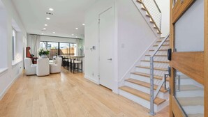 A spacious living area with a wooden floor, a staircase with metal railings, and a dining area with chairs and a table. - Oak Lawn Escape | Short Drive to Fair Park (Dallas)
