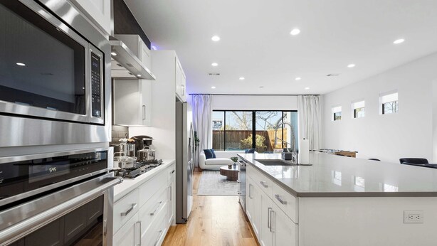 A modern kitchen with stainless steel appliances, a central island, and a view to a living area. - Trendy Oak Lawn Retreat | Near Fair Park (Dallas)