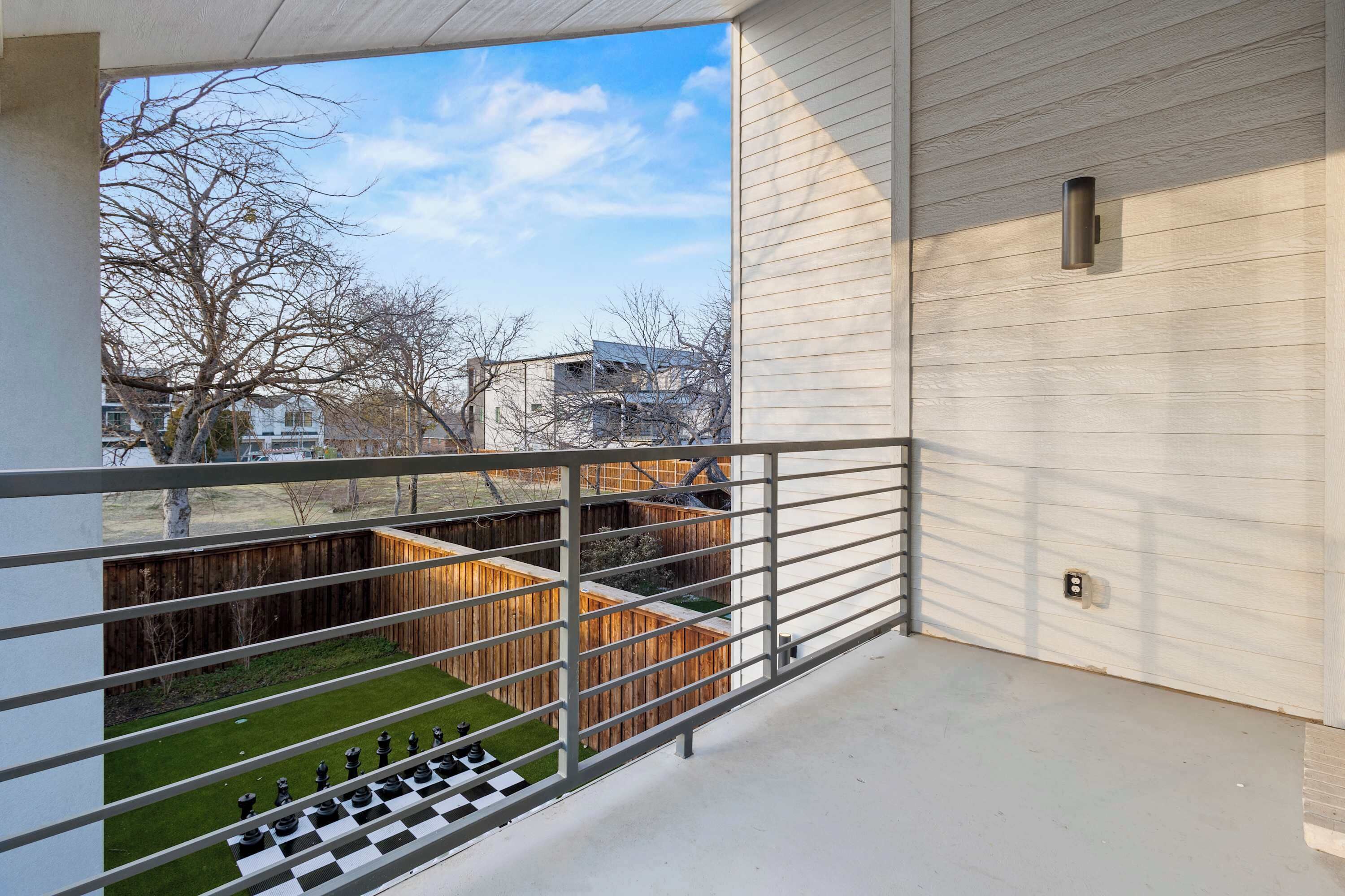 En balkon med skakbræt, et træhegn og udsigt til bygninger i baggrunden.