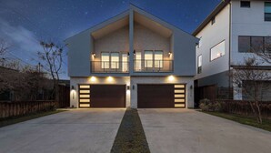 A modern two-story house with a garage, a central walkway, and a starry night sky. - Trendy Oak Lawn Retreat | Near Fair Park (Dallas)