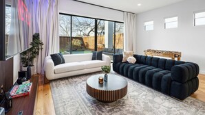 A modern living room with a white sofa, a dark sofa, a round coffee table, and a foosball table. - Trendy Oak Lawn Retreat | Near Fair Park (Dallas)