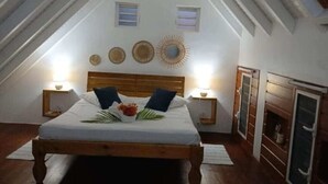Slaapkamer met schuine plafond, een houten bed, bedlampen, een tafeltje met een bloem en een spiegel aan de muur.