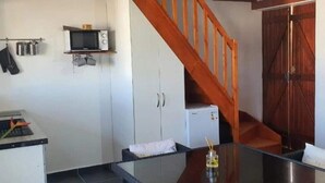 Een keuken met een magnetron, kastjes, een koelkast, een houten trap en een glazen tafel.